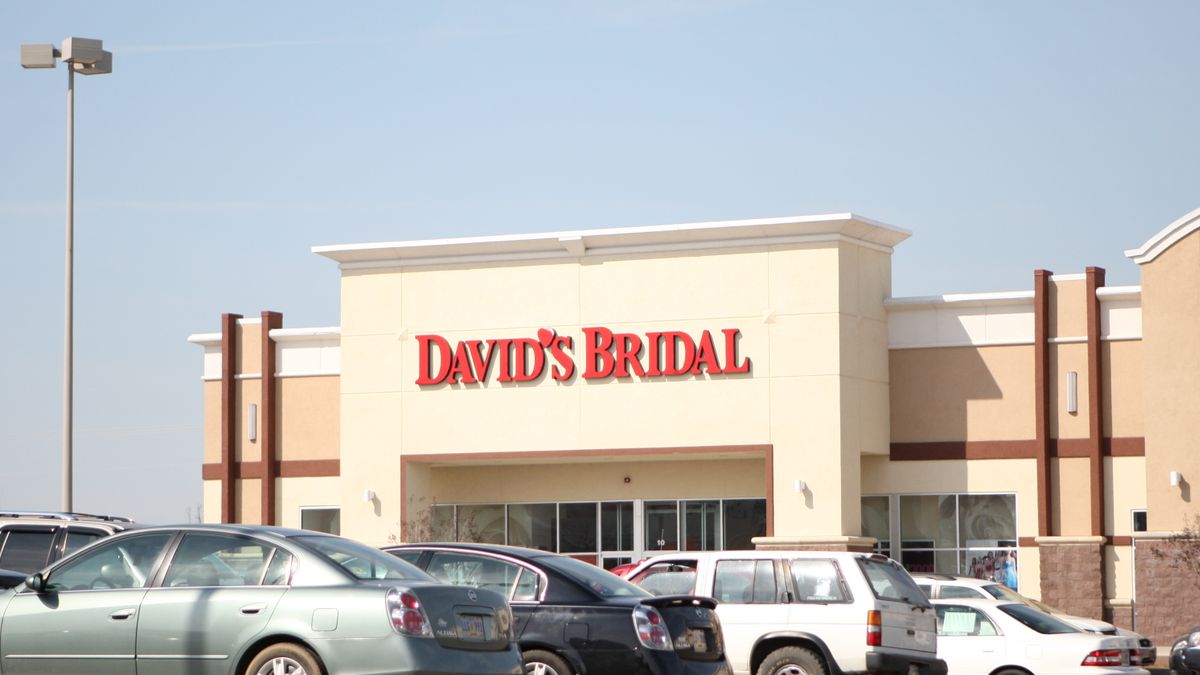 Cars parked in front of a David's Bridal store, against a pale blue sky.