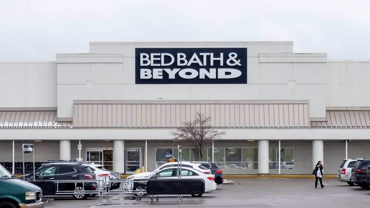 Cars are parked in front of a white building, against a white sky, with a dark blue banner that says "Bed Bath & Beyond" in white capital letters.