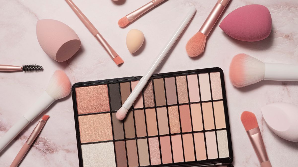 A nude eyeshadow palette and makeup artist's tools on a marble vanity. Brushes for powder, blush, eyebrows, shadows and sponges for concealer and foundation