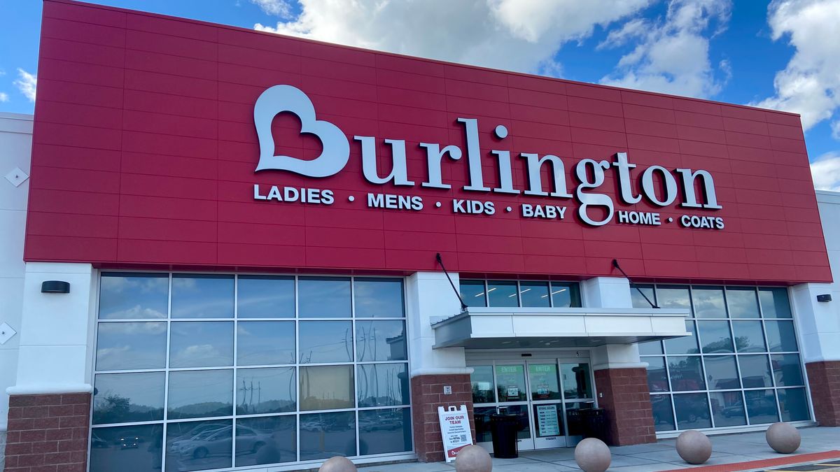 A red Burlington storefront says "ladies, mens, kids, baby, home, coats," as clouds billow overhead in a bright blue sky.