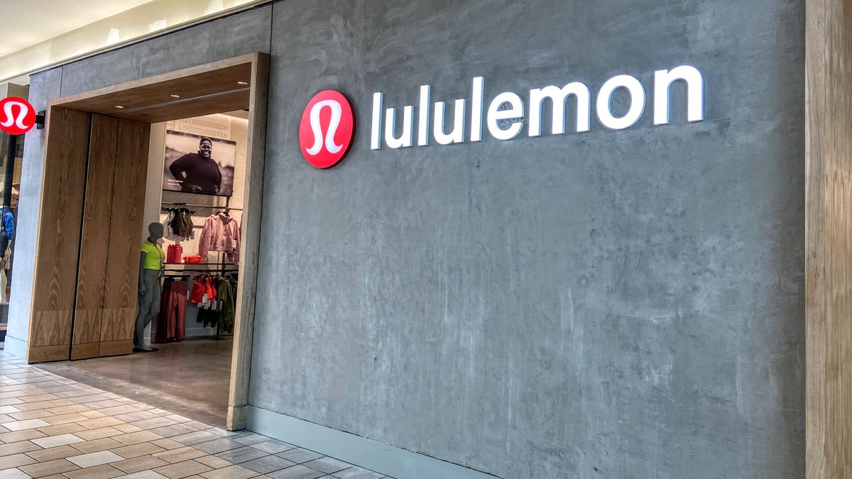 To the right of a mall store entrance, a minimalist gray granite facade features the red and white Lululemon logo and white lettering.