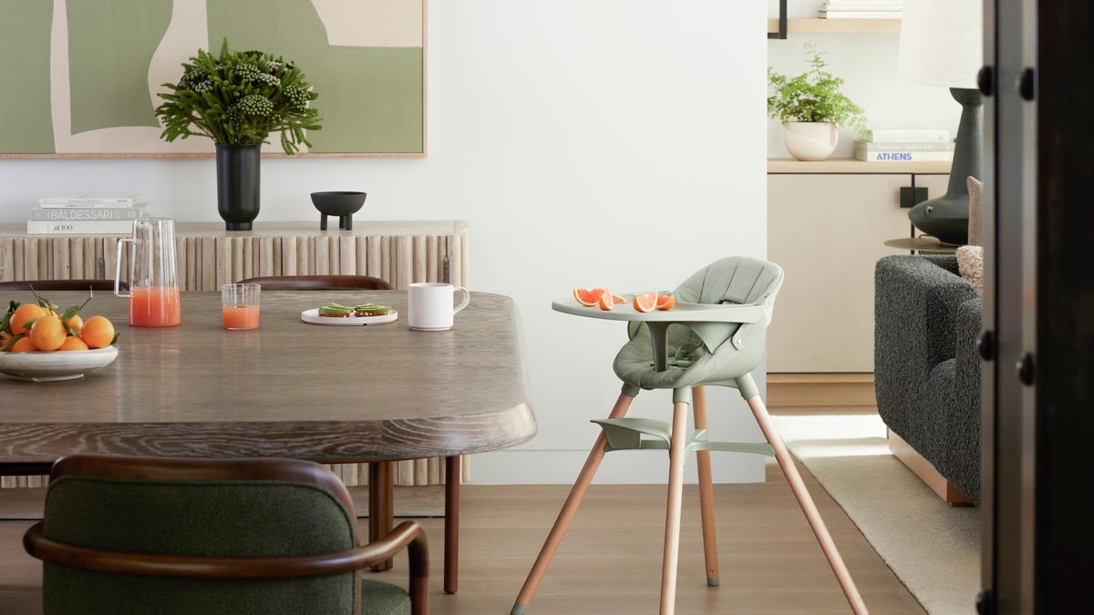A light sage green baby high chair displayed next to a wood table with fruits
