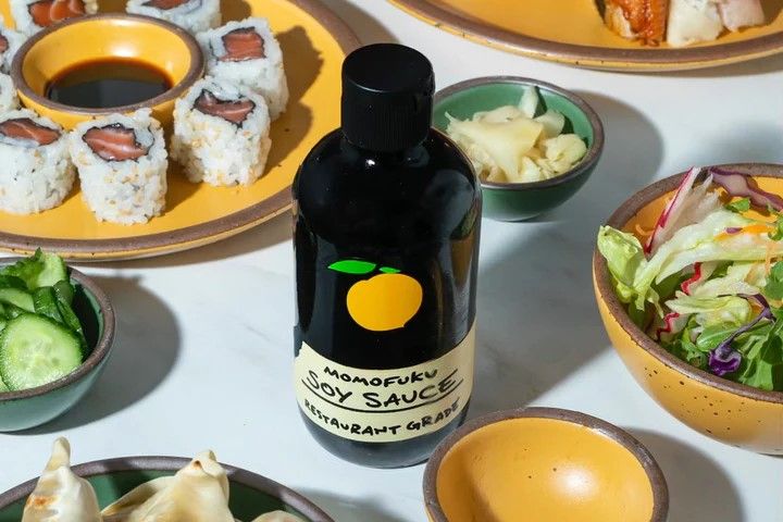 A clear soy sauce bottle with brown sauce on a table surrounded by food and plates