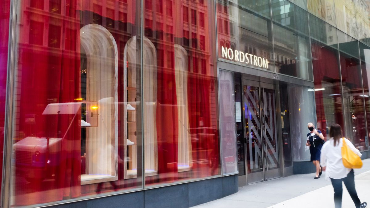 A pedestrian with a yellow bag walks by Nordstrom store windows decorated with red.