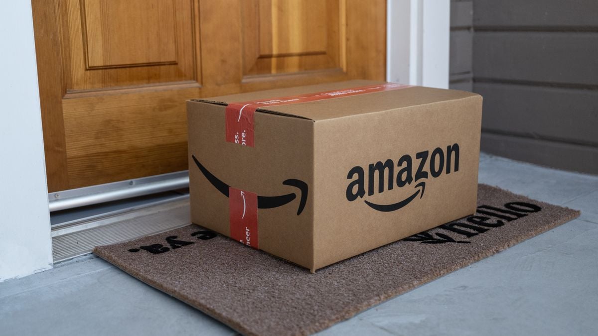 A large cardboard box sits on a welcome mat on the front porch of a house.