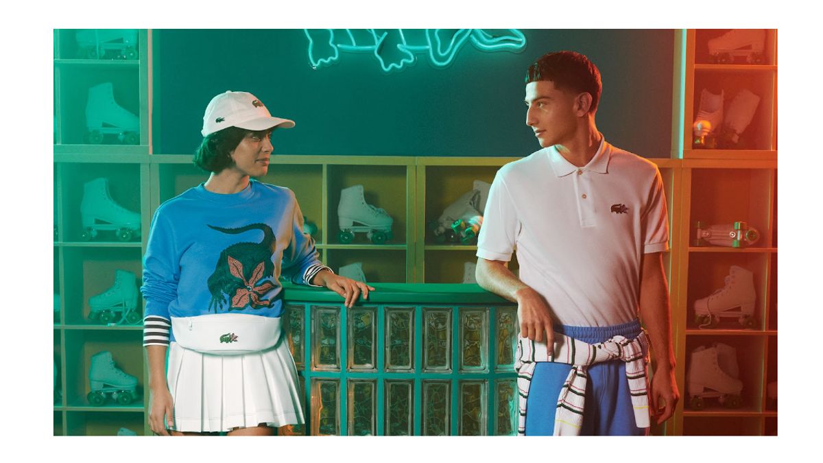 Two individuals wear Lacoste clothing in front of a wall of roller skates.