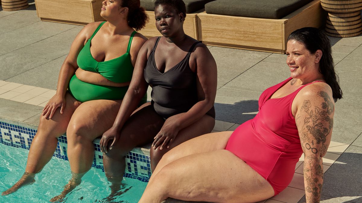 Three people sitting near a pool wearing items from Universal Standard's swimwear line.